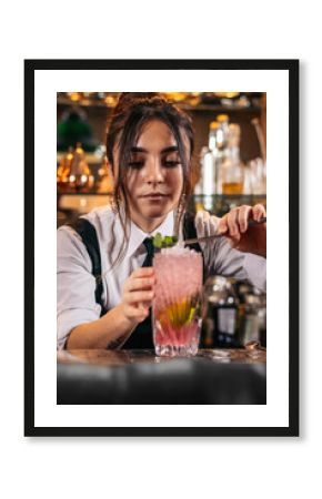 Female bartender pouring a cocktail and decorating it with garnish
