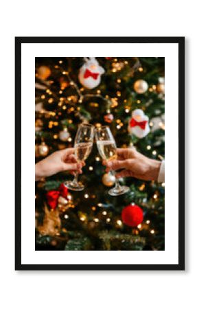 Two champagne flutes clink together in festive toast, with beautifully decorated Christmas tree and warm, twinkling lights in background. Concept of winter holidays, fun, celebratory events, party.