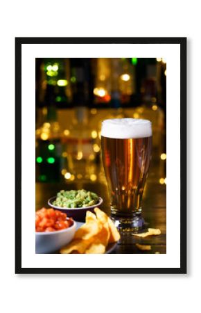 Glass of beer with nachos, tomato salsa and guacamole. Bar bottles in bokeh, high resolution