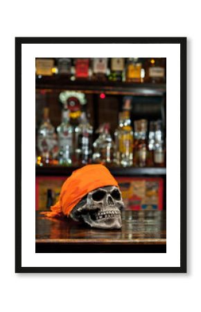 Human skull on a bar counter. Red skull in orange bandana on the background of bottles with alcohol. Biker Pub.