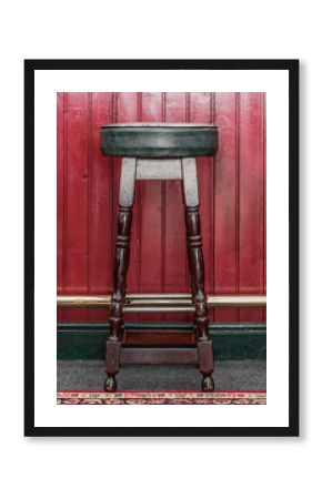 Vintage style wooden pub stool against a dark red wooden bar shot straight on.