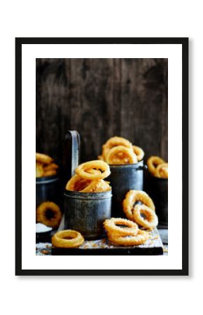 Crispy golden onion rings served in rustic metal cups on wooden surface