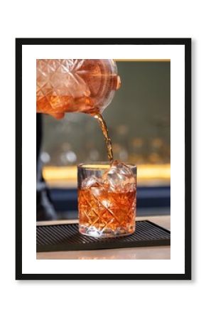 Bartender pouring cocktail into crystal tumbler with ice cubes