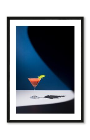 Bloody Mary decorado con hoja de apio en copa de cóctel sobre fondo azul 