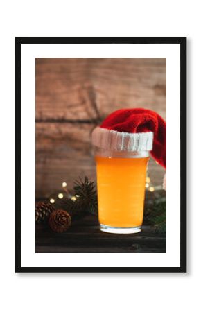 beer glass in a knitted Santa hat on a wooden table . Christmas ale, bokeh garlands, copy space