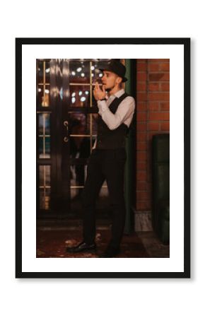 stylish man in a hat smokes a cigarette at door at entrance to bar