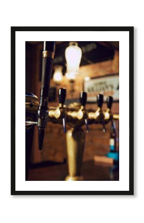 Close-up of row of shiny brass beer taps with handles, set against dark background with blurred bar counter. Vertical image. Concept of beer, brewery, pub, Oktoberfest, traditions