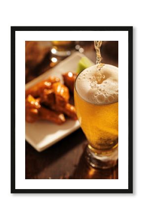 pouring beer with chicken wings in background.