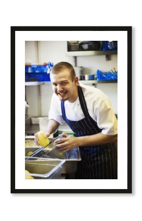 A village public house kitchen. A chef in apron working, using a mandolin cutter on potatoes. 