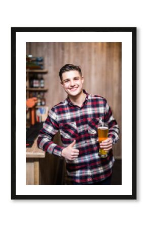 Handsome man holding a pint of beer with thumbs up at caunter in a pub