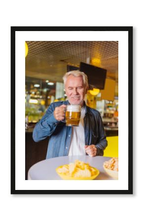 Favourite beer. Delighted aged man drinking beer while being in the pub