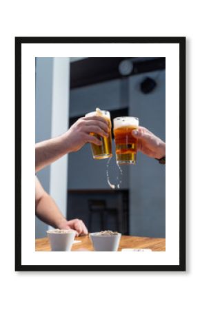 Men are clinking glasses with light beer over a table with beer snacks, in a pub with neon lights