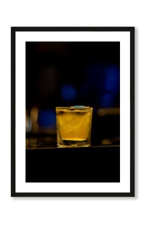Luminous yellow cocktail glowing on dark bar counter, blue lights blurring background, creating vibrant nightlife ambiance