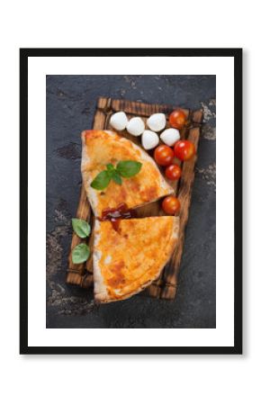 Sliced italian pizza calzone on a rustic wooden serving tray, flatlay on a brown stone background, vertical shot