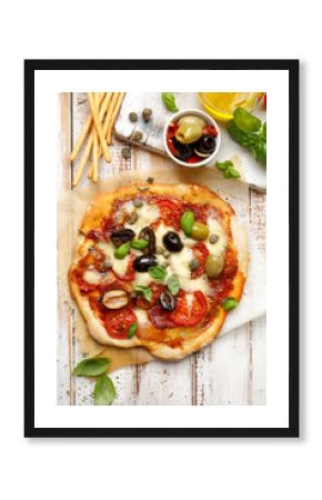 Homemade pizza with tomatoes, olives, salami, mozzarella cheese and fresh basil on a wooden rustic table, top view