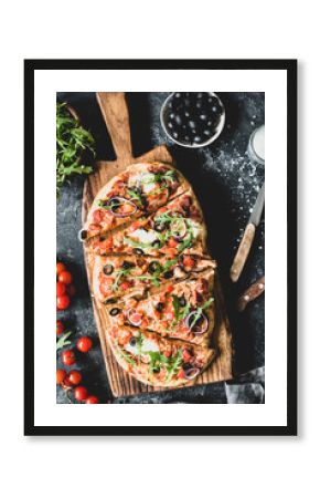Flatbread pizza garnished with fresh arugula on wooden pizza board, top view