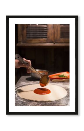Chef hand spreading tomato paste on pizza base