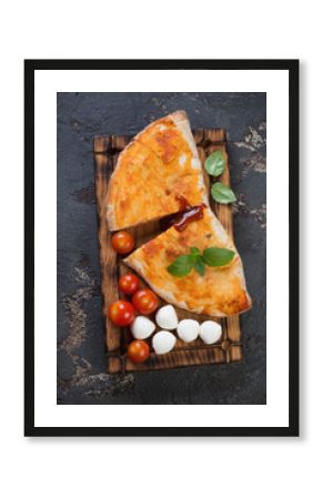 Rustic wooden serving board with sliced calzone pizza, view from above on a brown stone surface, vertical shot