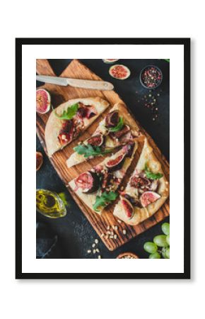 Pizza or flatbread with fig, prosciutto, parmesan cheese, arugula on wooden cutting board, top view