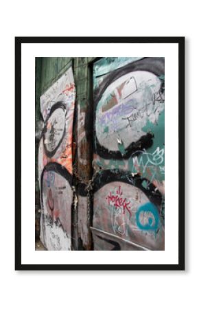 Close-up of an aged green wooden door covered in layered graffiti, featuring a rusted chain and padlock that highlight its urban decay and textured street-art character.