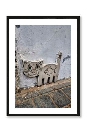 A cute metal plaque shaped like a cat with a fish symbol attached to a weathered wall in St. Petersburg.