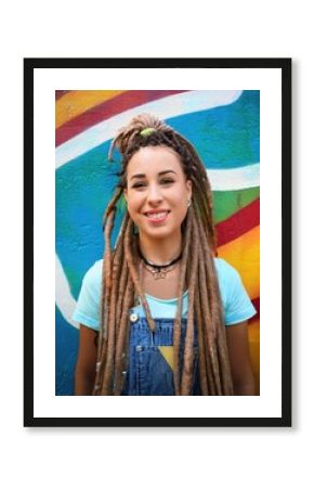 Young woman with long dreadlocks and nose piercing smiling against a vibrant graffiti background 