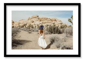 Woman in boho style dress and hat rushing through the Joshua Tree desert landscape