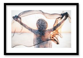 Beautiful boho girl with her hands raised up holds a silk scarf on breeze. Handsome woman look on evening sun on horizon