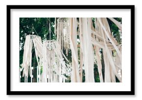 Stylish boho decor on trees. Modern bohemian decoration of white macrame and ribbons, hanging on branches in summer park. Wedding decor and arrangement. Stylish arch for ceremony