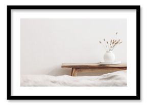 Modern white ceramic vase with dry Lagurus ovatus grass and marble tray on vintage wooden bench, table. Blurred beige linen blanket in front. Scandinavian interior. Empty white wall, copy space.