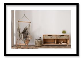 Empty wall in modern child room. Mock up interior in boho style. Copy space for your picture or poster. Wooden sideboard, rattan basket, hanging armchair, toys. Cozy room for kids. 3D rendering.
