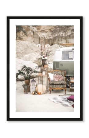 Green hippy bus, vintage armchair with pillows, retro radio, golden metal decorations with plants, succulents, flowers and candles, fur carpet on the background of desert landscape. Boho decor
