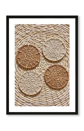 Four round woven rattan coasters displayed on a larger woven mat in a natural, earthy color palette.