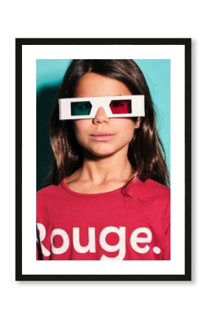 Portrait of happy preteen girl in white plastic stereoscopic glasses with red and blue lens smiling at camera while watching 3d graphic film with pleasure against turquoise background in modern studio