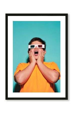Shocked surprised preteen boy with mouth opened in special glasses with stereoscopic blue and red lens looking away and enjoying 3d graphic video against turquoise background in modern studio