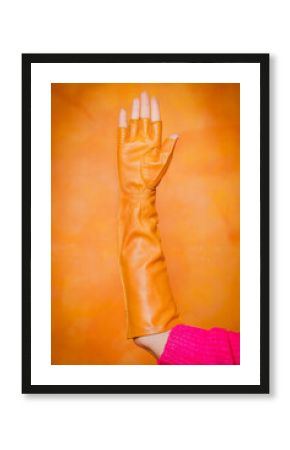 Yellow long mitten gloves on a woman's hand on an orange background