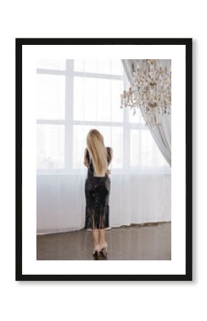 Back view of a woman in black dress with long blond hair at the window.