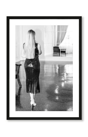 Back view of a woman in black dress with long blond hair in the room. Monochrome photo.