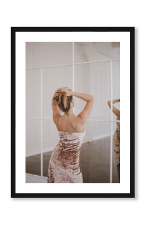 Back view of a blond woman in beautiful dress looking in the mirror.