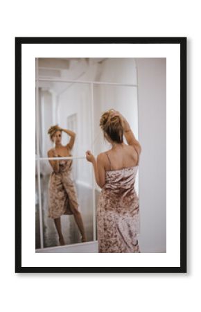 Back view of a blond woman in beautiful dress looking in the mirror.