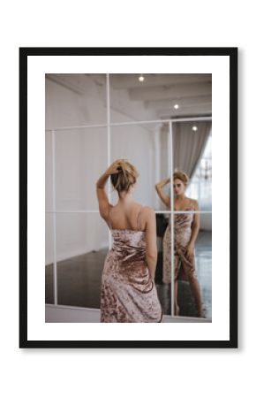 Back view of a blond woman in beautiful dress looking in the mirror.