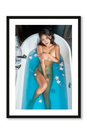 Young naked woman sitting in white bath with blue water