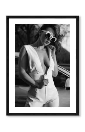 Young rude hair woman in sunglasses posing in sexy elegant white trousers costume  during the evening sunset  