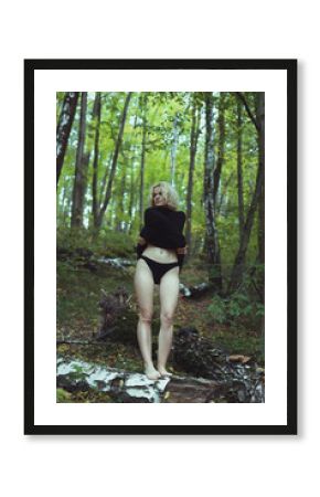 Blonde model taking off clothes in wood scenic photography. Picture of person with wild forest on background. High quality wallpaper. Photo concept for ads, travel blog, magazine, article