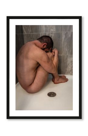 depressed, anxious, or sad man naked sitting in shower as water runs over bare skin and face