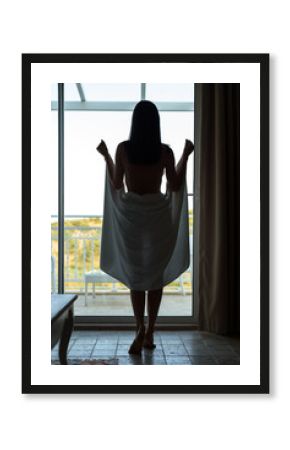 Silhouette of a half-naked woman with a towel in front of the panoramic window of the room