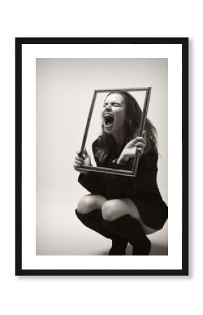 Young girl in a jacket looking through the picture frame and screaming