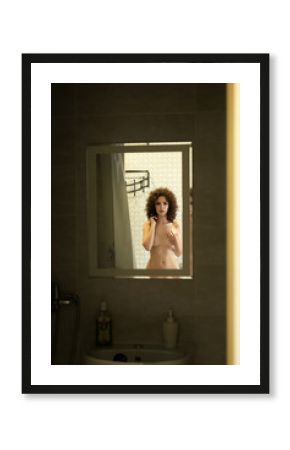 Beautiful naked girl looks at her reflection in the bathroom mirror
