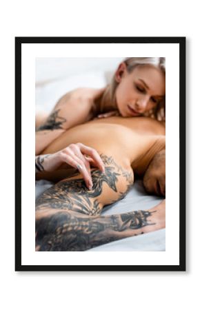Selective focus of naked girl touching shirtless tattooed boyfriend on bed isolated on white