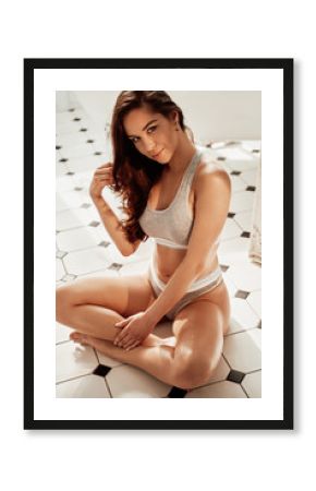 Close-up view of an attractive female model with dark hair posing in a bathroom wearing grey fitness lingerie